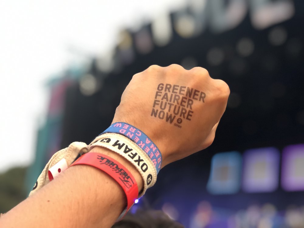 A hand stamped with the message 'greener, fairer future now' making a fist in a festival crowd