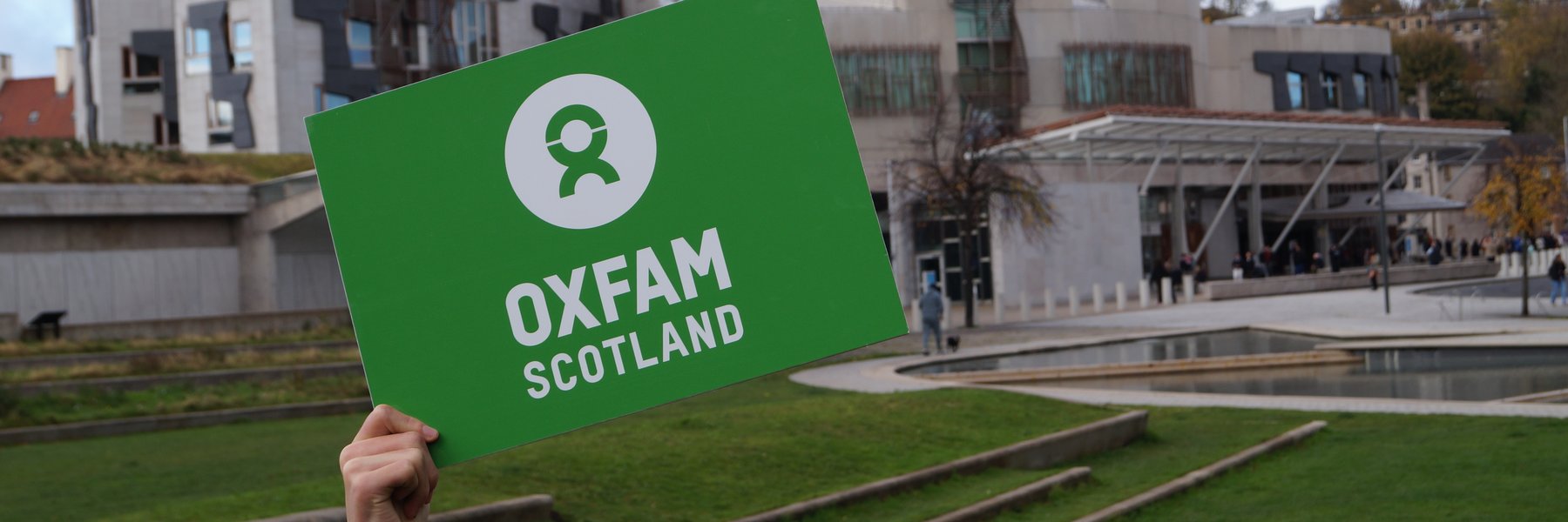 Green banner reading Oxfam Scotland held in front of Scottish Parliament