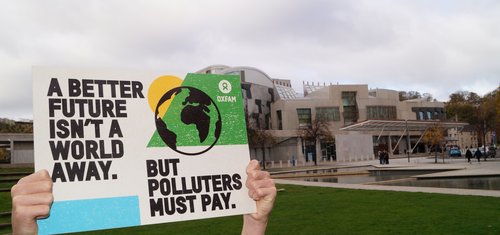 A placard being held aloft with the text 'A better future isn't a world away, but polluters must pay'