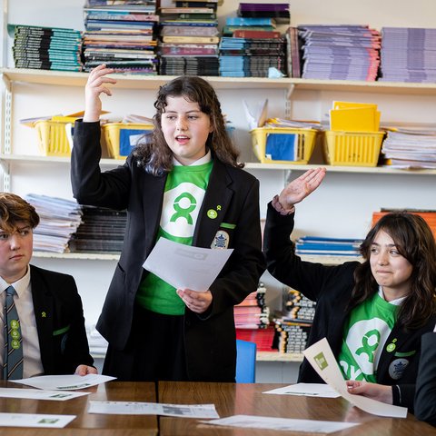 School kids in green Oxfam t-shirts raise their hands.