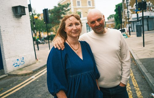 A man and woman stand outside on a residential London street.