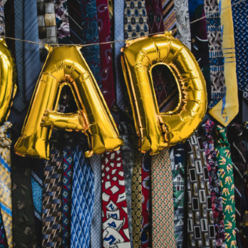 Gold balloons spelling out DAD, on a background of funky pattern ties all hung up. Two rows of around 40 ties.