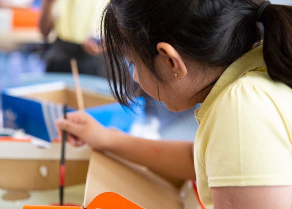 A girl paints a shoe box that she is making into a dolls' house to show what home means to her.