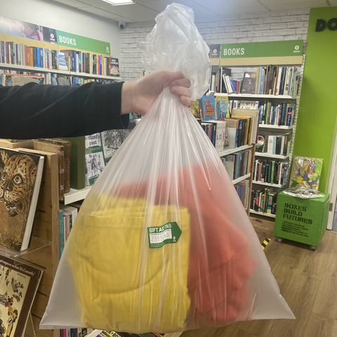 Someone holds a bag of donations, with a Gift Aid sticker attached. Oxfam branding and books can be seen in the background.