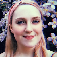 A photo of Ella Maskery, a white woman with blue eyes in her 20s with purple flowers in the background.