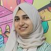 Fatema, a woman in a pale grey headscarf, smiles as she poses for photo.