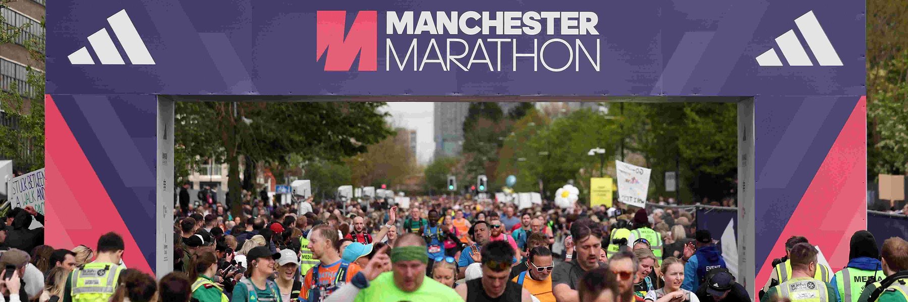 Runners cross the finish line at the Manchester Marathon under a large purple banner, surrounded by cheering crowds and event staff.
