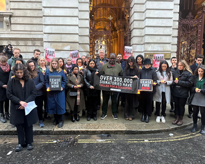 A group of people stand outside Downing Street looking downcase holding a banner about 300,000 people signing a ceasefire petition.