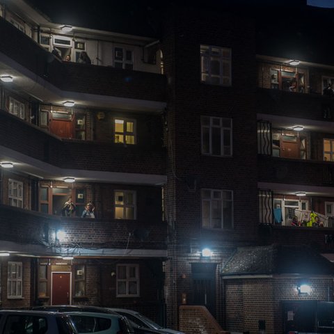 A UK council estate block of flats at night with some people on the balconies