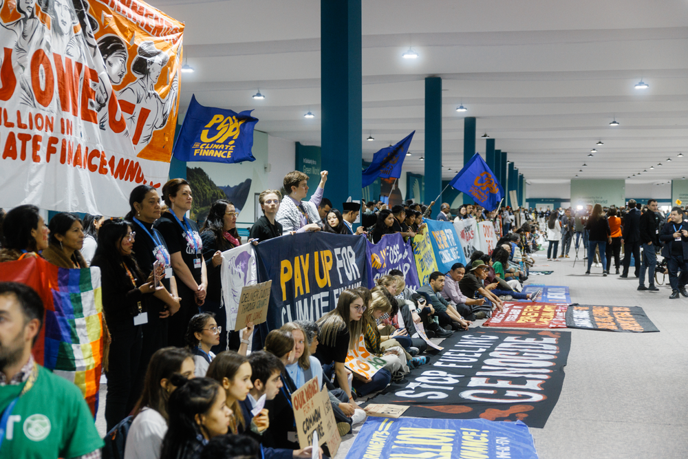 Large number of activists with Make Polluters Pay banners along a long corridor at COP29