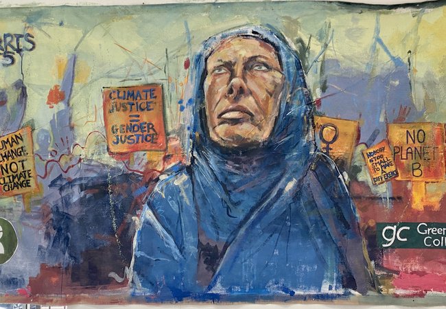 A painting of a woman in blue hijab looking to the sky with banners behind her saying 'human change not climate change' and 'climate justice = gender justice' and 'no planet B'