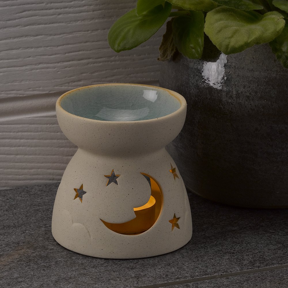 stone coloured oil burner with moon and stars cut out photographed next to a plant