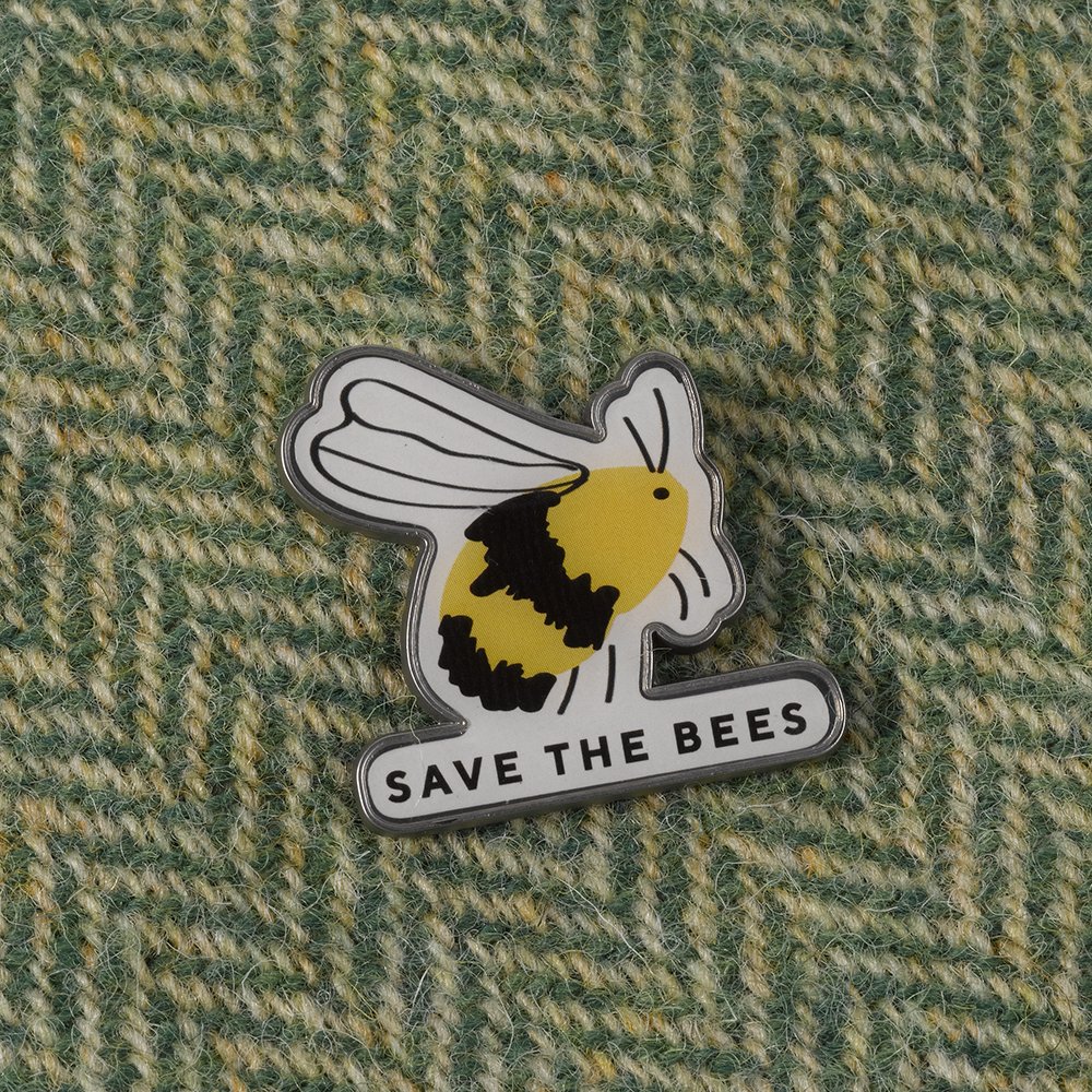 A metal badge with an illustration of a bee that says save the bees pinned to green wool material