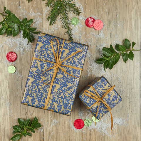 Dark blue and gold design wrapped Christmas gifts with ribbon with red divine gold chocolate coins and sprigs of greenery.