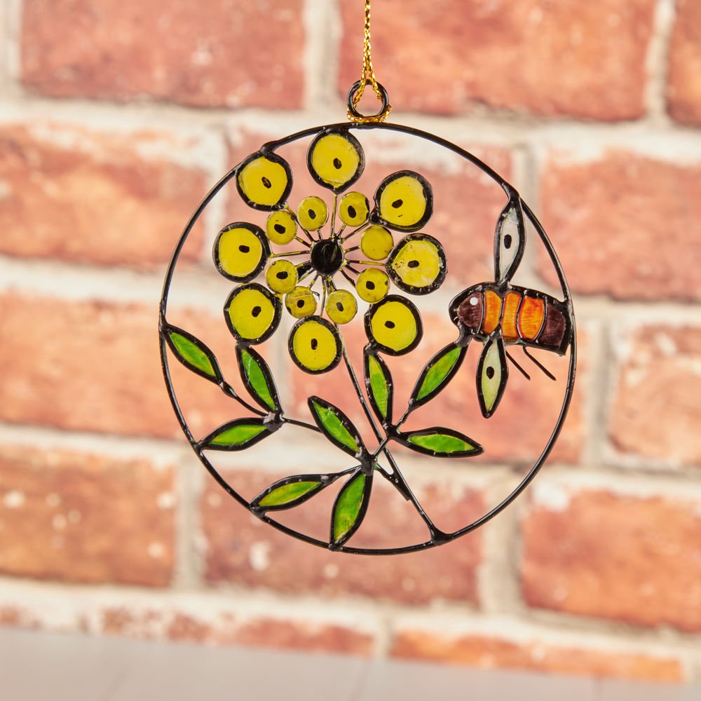 small glass bee and flower hanging decoration in front of a brick wall