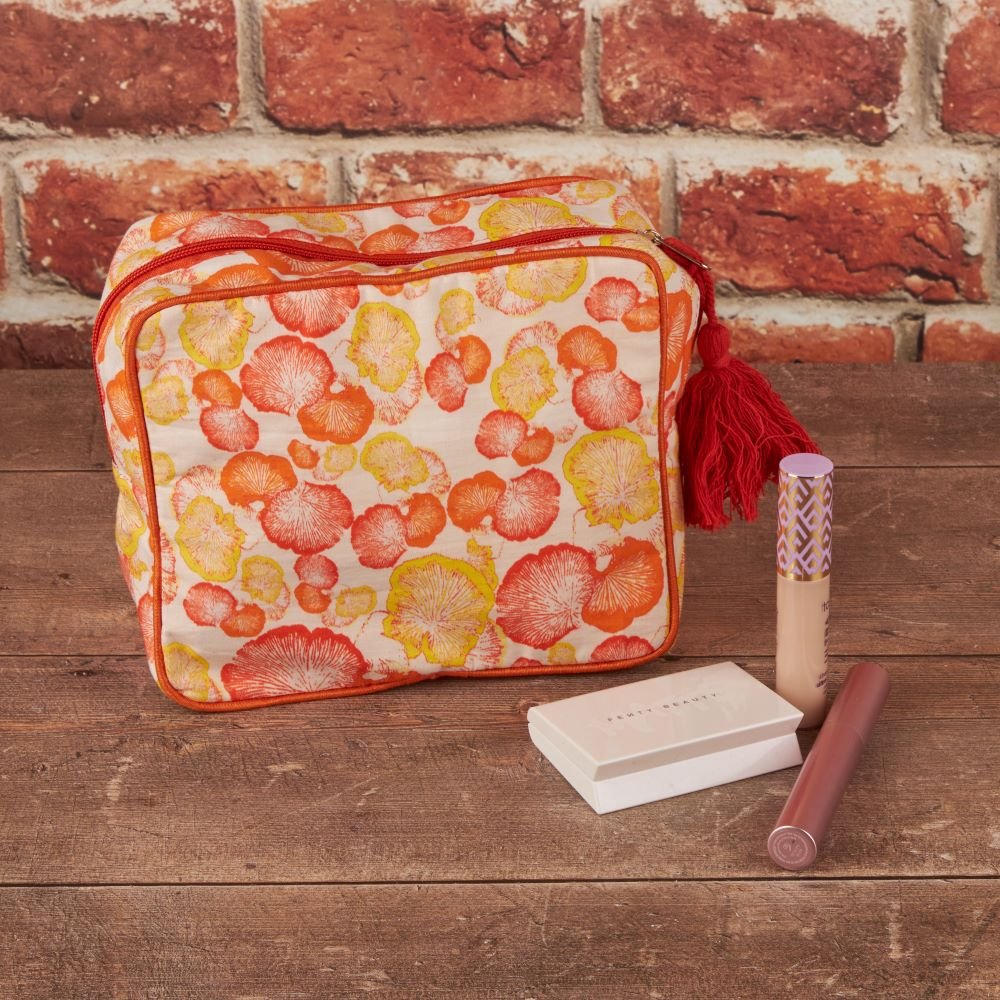 makeup bag with yellow and orange mushroom print on a wooden table with makeup items next to it