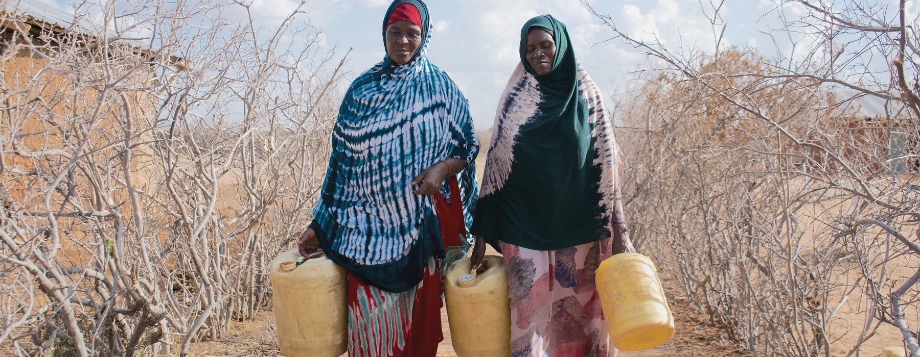 Hadija Jillo and another woman walking to fill up yellow jerry cans on parched ground