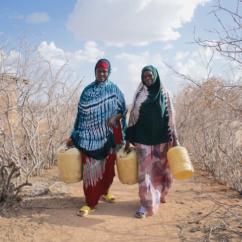 Hadija Jillo and another woman walking to fill up yellow jerry cans on parched ground