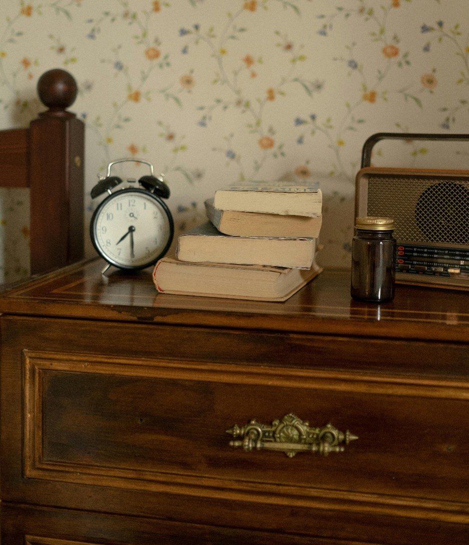 Small alarm clock, books and a retro radio placed on a chest of wooden draws.