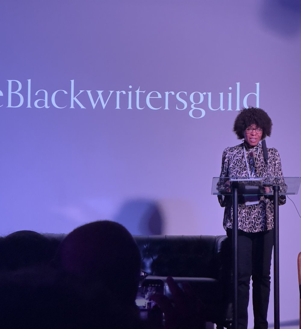 Margaret Busby stands and speaks in front of a screen displaying 'The Black Writers Guild' text.
