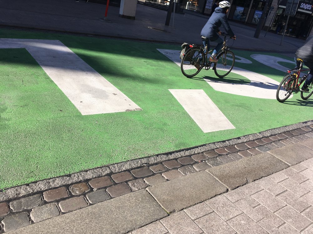 People cycling over a green painted road with 1.5 degrees C written on it.