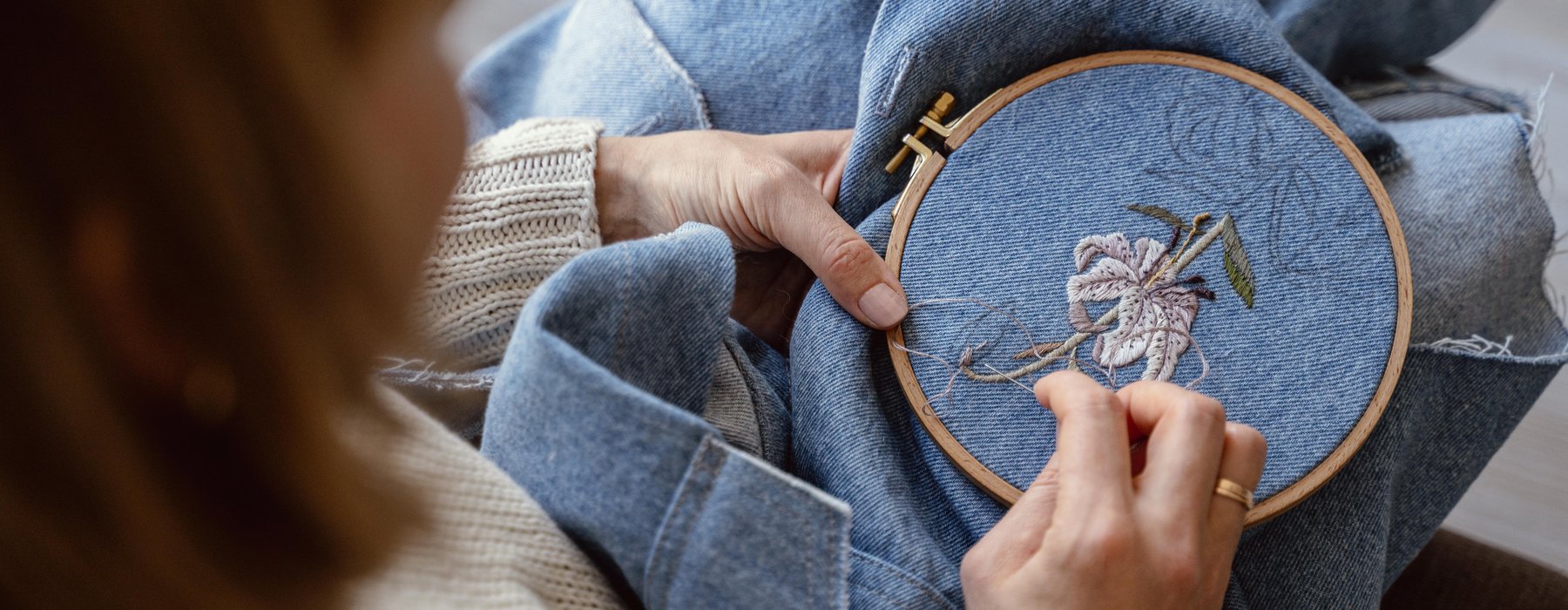 A person adding an embroidery flower to a denim piece of clothing.