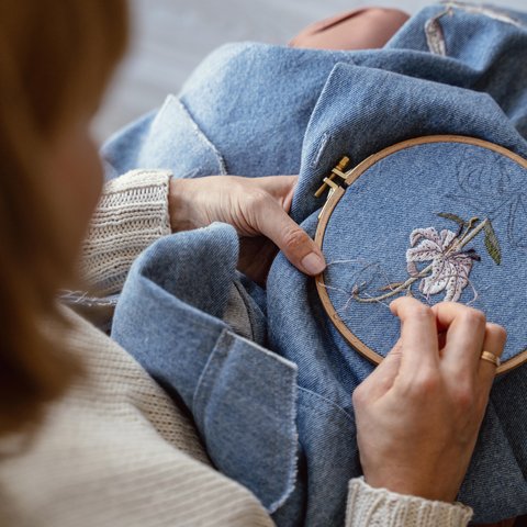 A person adding an embroidery flower to a denim piece of clothing.