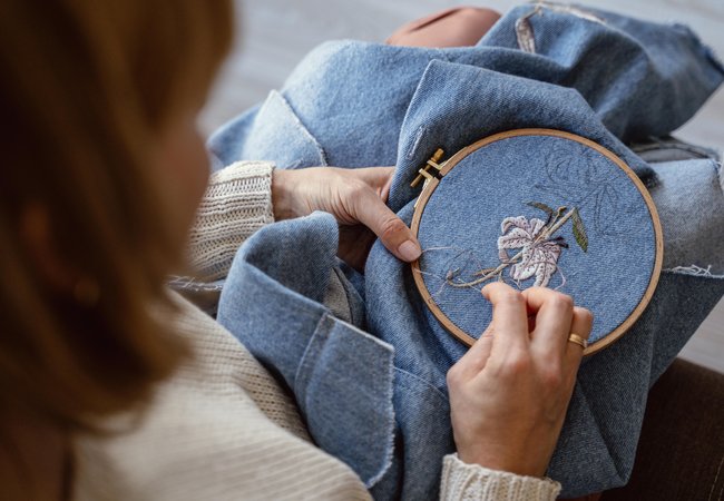 A person adding an embroidery flower to a denim piece of clothing.