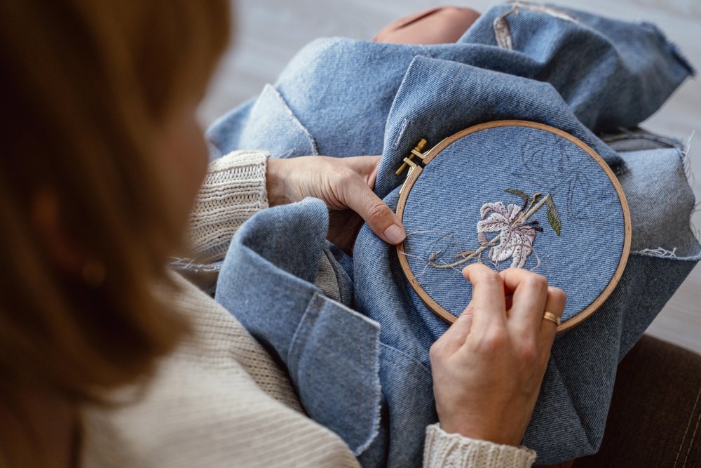 A person adding an embroidery flower to a denim piece of clothing.