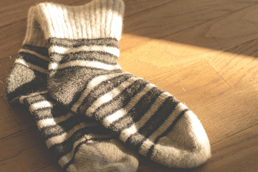 A pair of grey, black and white stripy fluffy socks on a wooden floor.