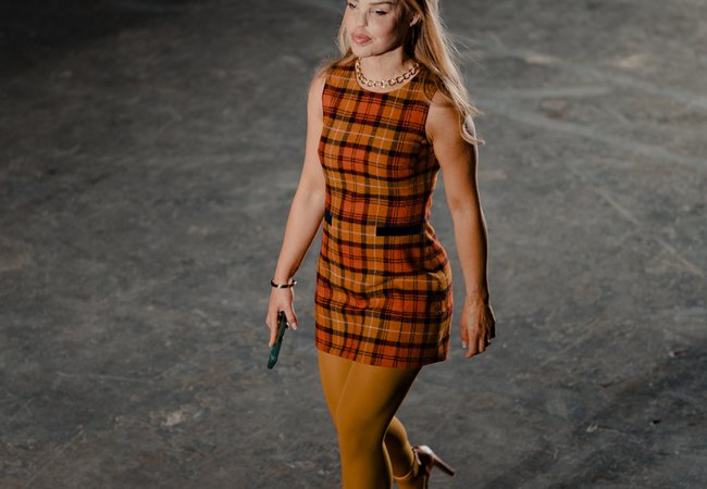 Katie Piper walking the catwalk at the Oxfam x Vinted Style for Change fashion show. She wears an orange checked mini dress, mustard tights and orange platform heels.