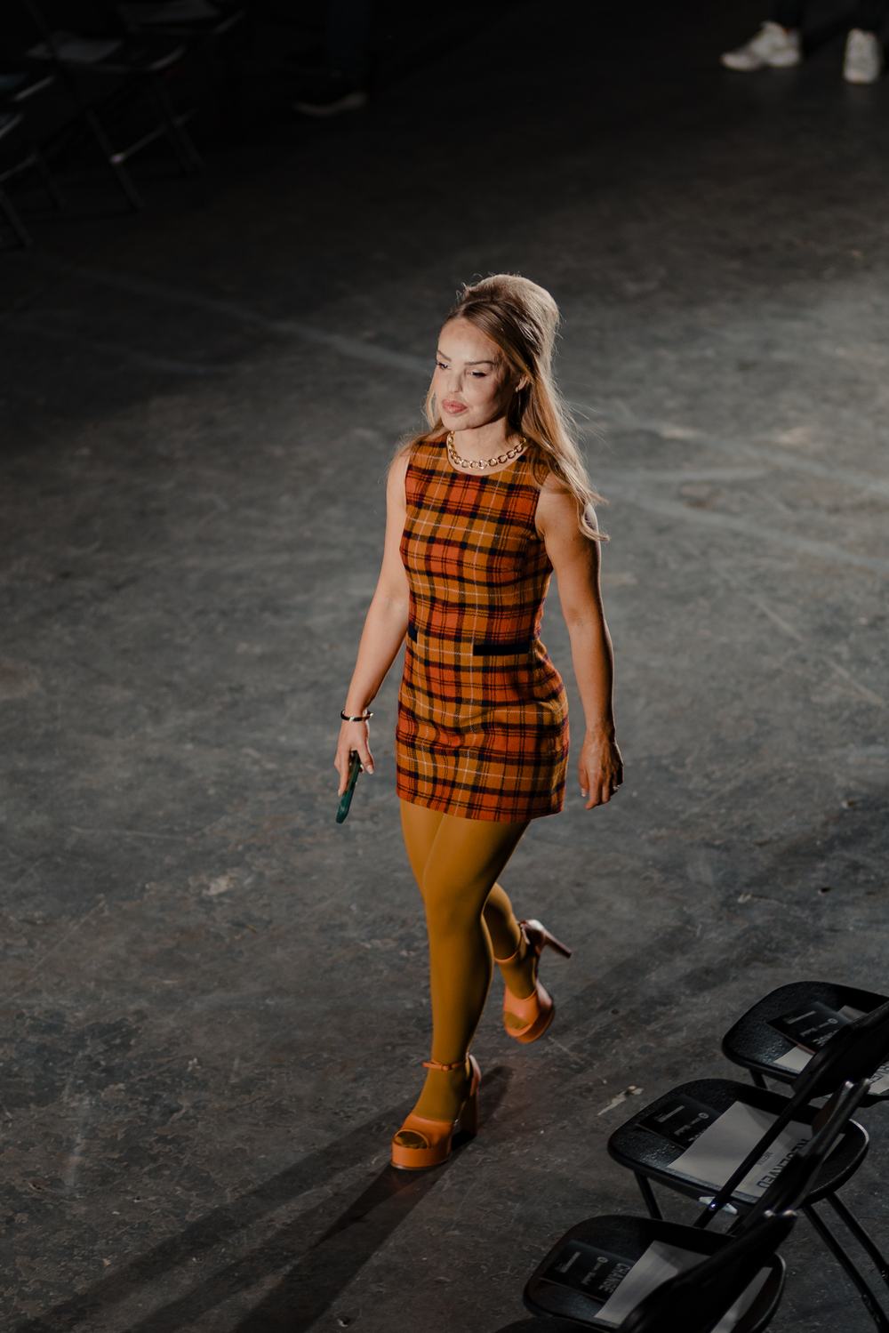 Katie Piper walking the catwalk at the Oxfam x Vinted Style for Change fashion show. She wears an orange checked mini dress, mustard tights and orange platform heels.