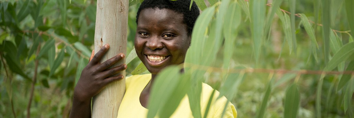 Jessy, a climate activist from Malawi, stands smiling next to a tree.