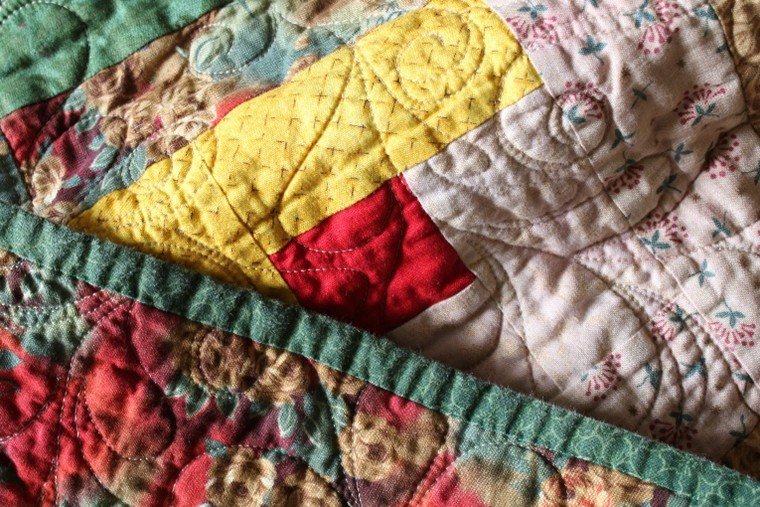 A close up shot of a patchwork quilt showing different fabrics, textures and patterns