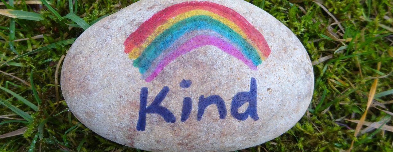 A pebble painted with a rainbow and the word 'Kind'.