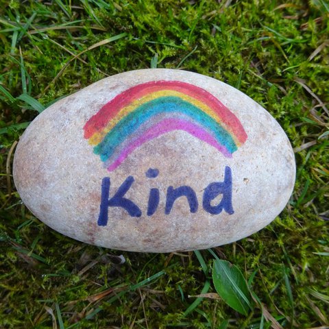 A pebble painted with a rainbow and the word 'Kind'.