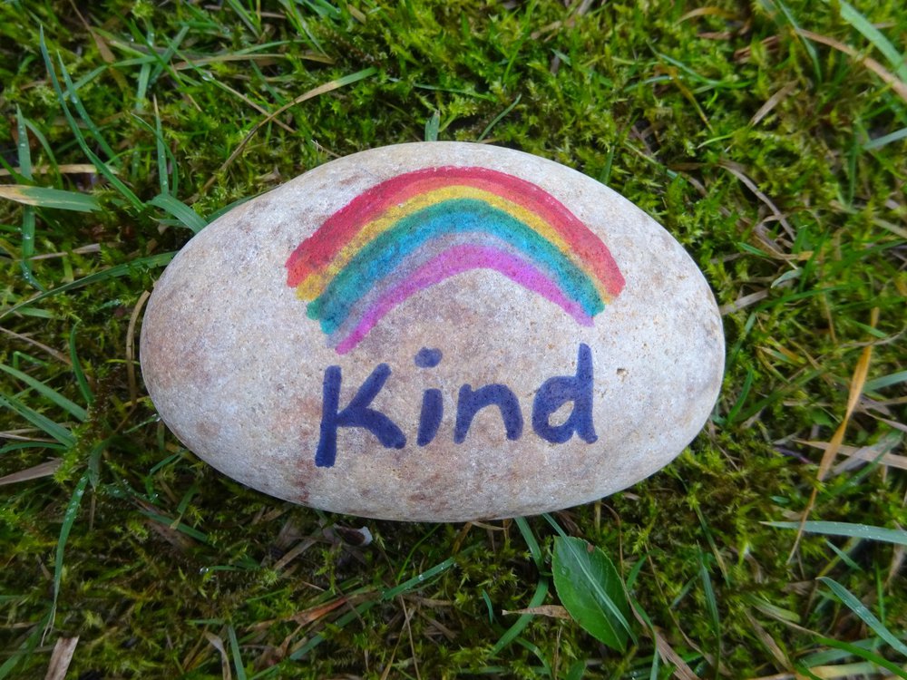 A pebble painted with a rainbow and the word 'Kind'.