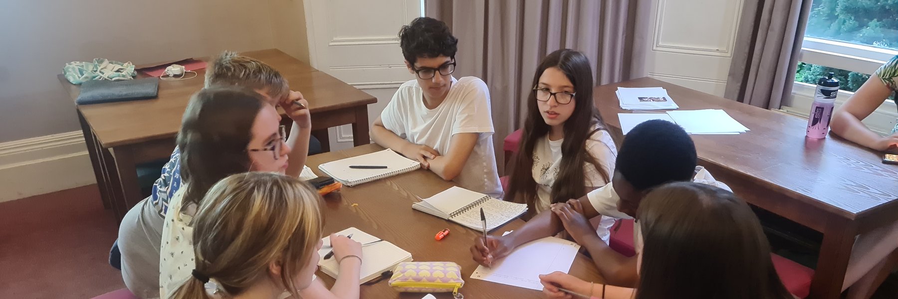 Seven young people plan a project sitting at a table with notepads and pens.