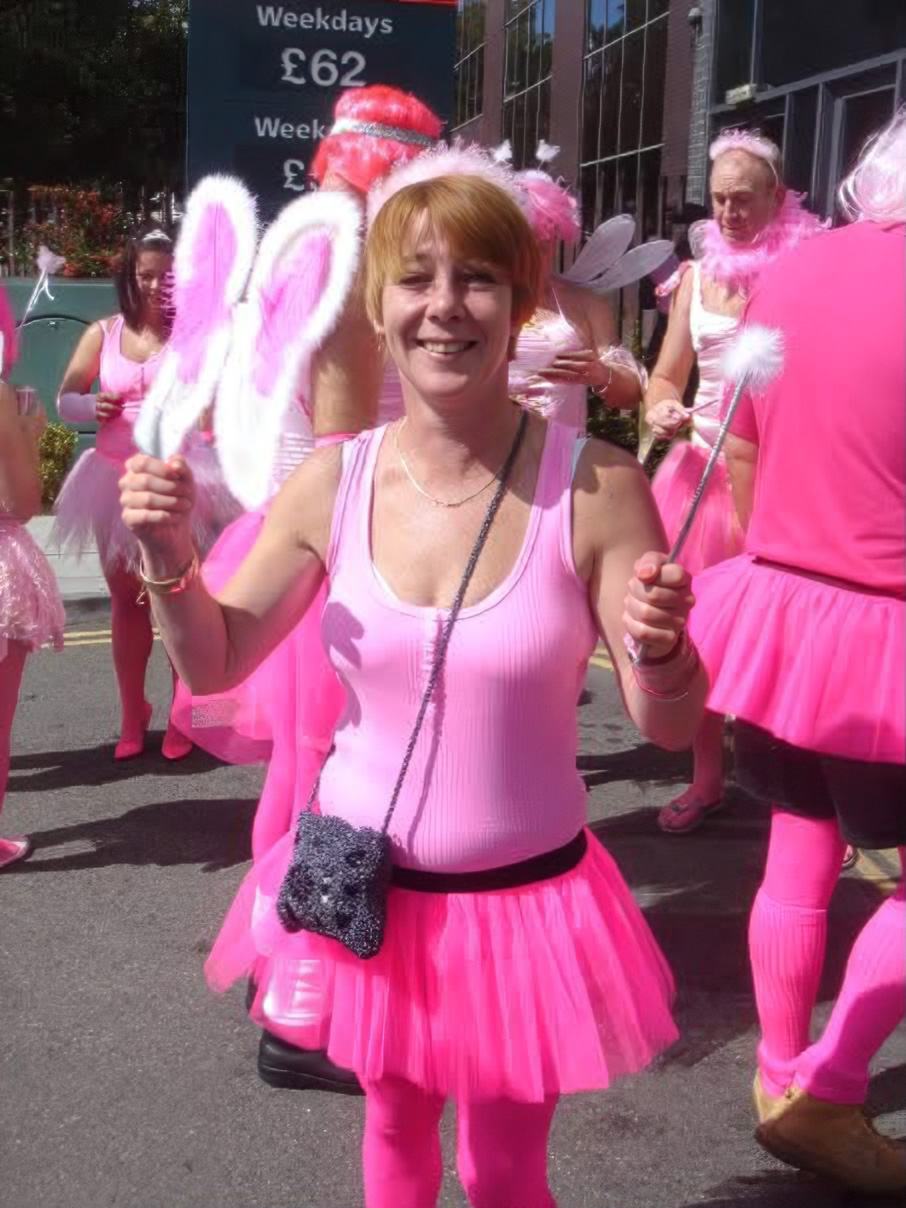 Lisa is outside a venue wearing a pink leotard and pink tutu skirt with other people in the background dressed in similar clothes.