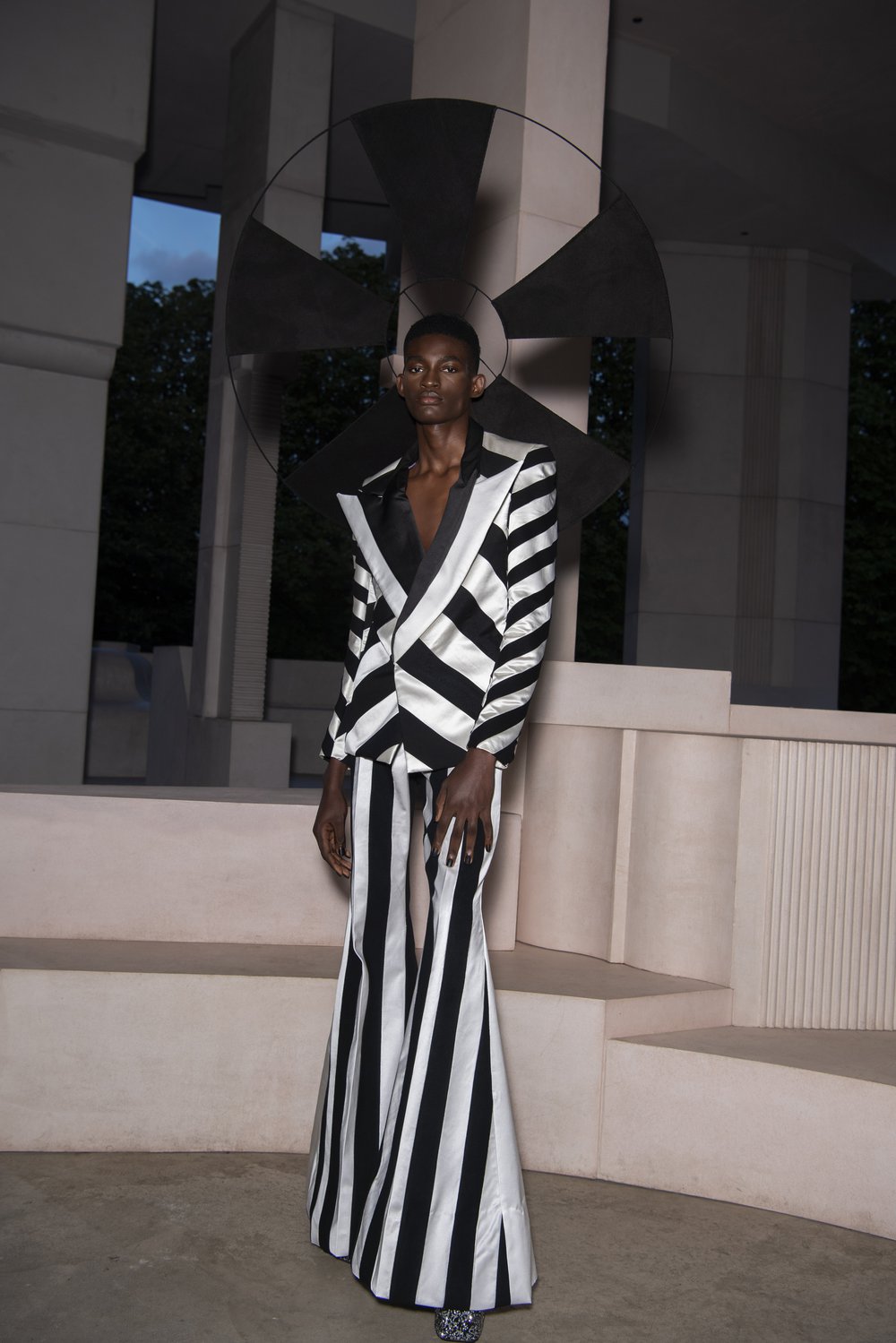 A model wears a black and white wide-striped satin suit made from pre loved Oxfam bridal wear and a black halo