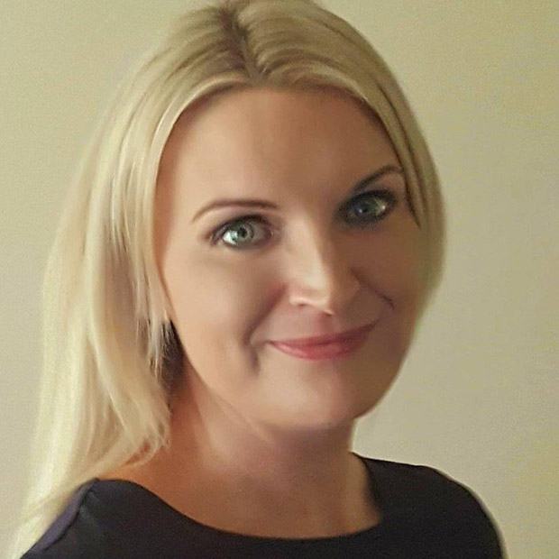 Person with long blonde hair wearing a dark top, shown from the shoulders up.