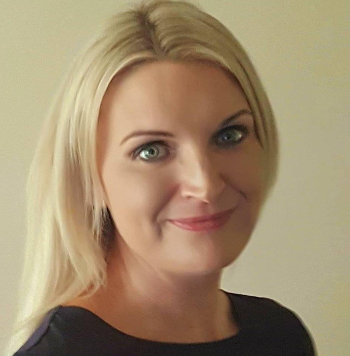 Person with long blonde hair wearing a dark top, shown from the shoulders up.