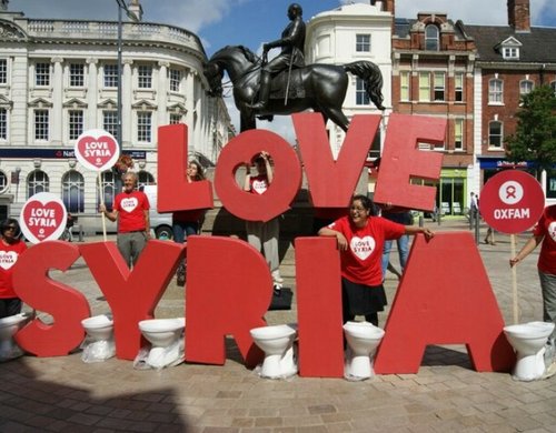 Campaigners in red Oxfam t-shirts stand next to huge letters spelling out the words 'Love Syria'