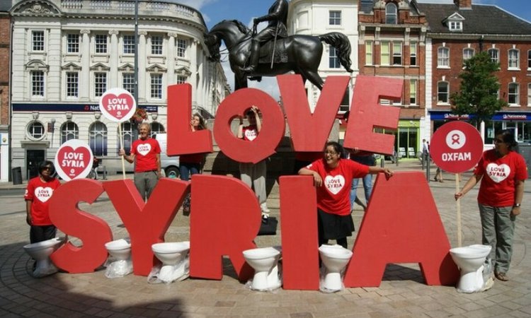 Campaigners in red Oxfam t-shirts stand next to huge letters spelling out the words 'Love Syria'
