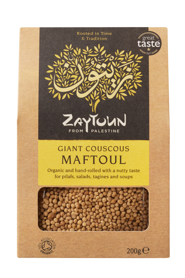 a paper bag of Zaytoun giant couscous maftoul. The front has a transparent panel so you can see the beige couscous grains inside the packaging. The packaging features the Fairtrade logo