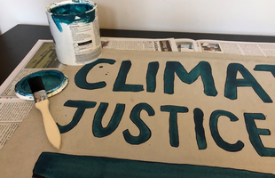 Blue paint, a paintbrush and a finishes sign that says 'climate justice now'