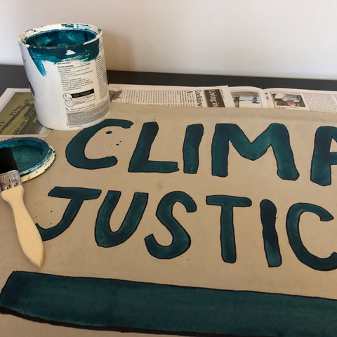 Blue paint, a paintbrush and a finishes sign that says 'climate justice now'