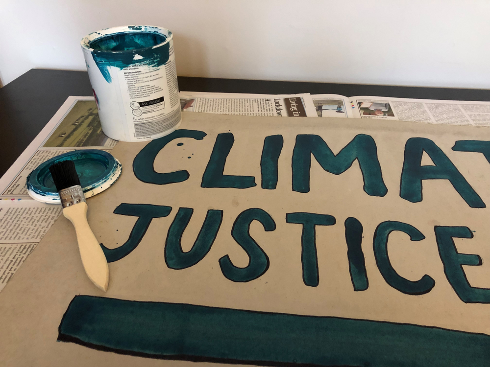 Blue paint, a paintbrush and a finishes sign that says 'climate justice now'