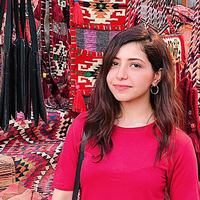 A portrait of Armanos wearing red and standing by a stall selling colourful fabric