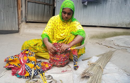 A woman sat on the ground, crafting a woven basket.